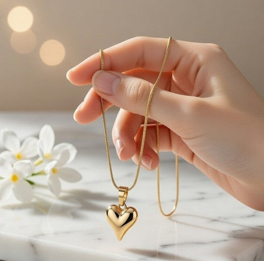 Hand holding a gold heart-shaped necklace on a marble surface with white flowers.