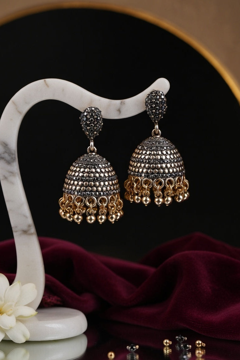 Pair of gold and silver jhumka earrings on a white marble stand with a dark background.